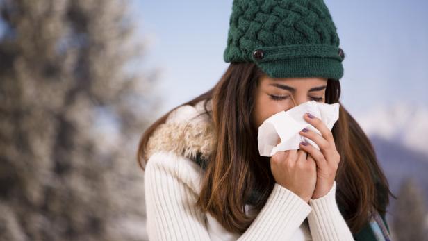 Eine Frau mit Mütze putzt sich bei kaltem Wetter die Nase.