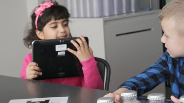 Ein Mädchen mit einem rosa Stirnband benutzt ein Tablet, während ein Junge zusieht.
