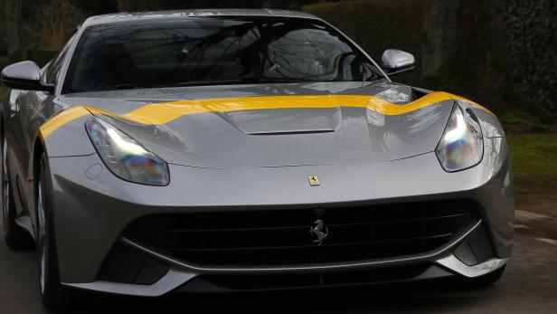 Ein grauer Ferrari mit gelbem Streifen fährt auf einer Straße.