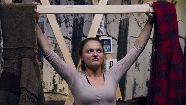 Eine Frau hält eine Holzstange mit einem braunen und einem rot karierten Kleidungsstück daran.