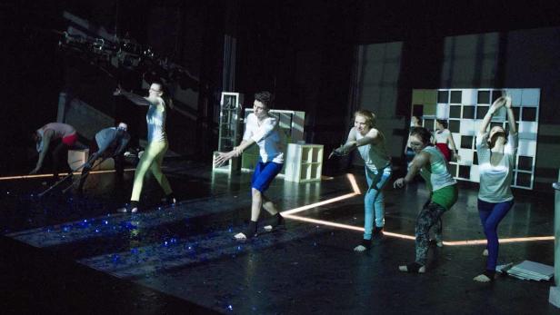 Mehrere Tänzerinnen und Tänzer treten auf einer Bühne mit minimalistischem Bühnenbild auf.