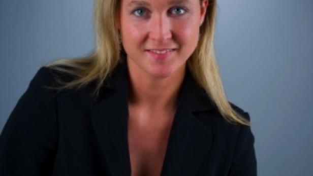 Eine Frau mit blonden Haaren und einem schwarzen Blazer lächelt in die Kamera.