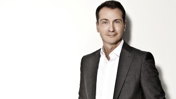 Ein Mann mit blauen Augen trägt ein graues Jackett und ein weißes Hemd.