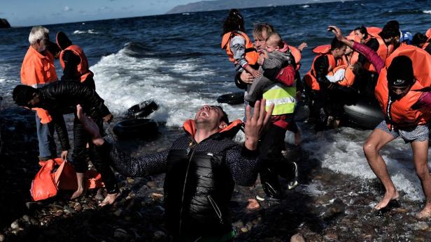 Menschen in Schwimmwesten steigen aus einem Schlauchboot an einem steinigen Strand.