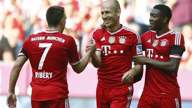Drei Fußballspieler des FC Bayern München in roten Trikots umarmen sich.