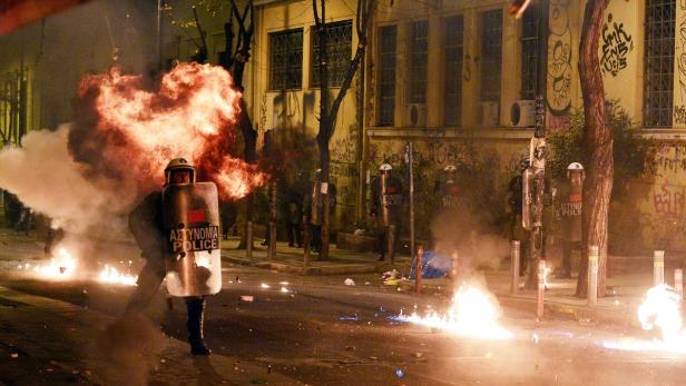 Ein Polizist mit Schutzschild steht inmitten von Rauch und Flammen auf einer Straße.