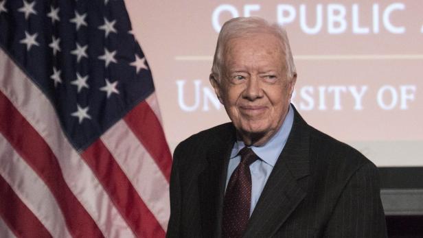 Jimmy Carter steht vor einer US-Flagge.