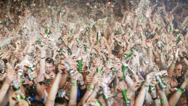 Eine Menschenmenge feiert mit erhobenen Bierdosen, aus denen Flüssigkeit spritzt.