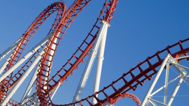 Eine rote und weiße Achterbahn vor einem strahlend blauen Himmel.