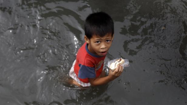 epa03832027 A Filipino boy holding a sandwich wades through floodwaters in Muntinlupa city, south of Manila, Philippines, 21 August 2013. Floods reaching as high as two metres swamped a wide area in the northern Philippines, including Manila, after days of heavy rains, killing 14 people. More than one million people were affected, including 281,126 people forced to stay in emergency shelters or with family and friends, according to the National Risk Reduction and Management Council. The monsoon rains in the Philippines were being enhanced by tropical storm Trami, which was moving towards Taiwan with maximum sustained winds of 105 kilometres per hour (kph) and gusts of up to 135 kph. EPA/FRANCIS R. MALASIG
