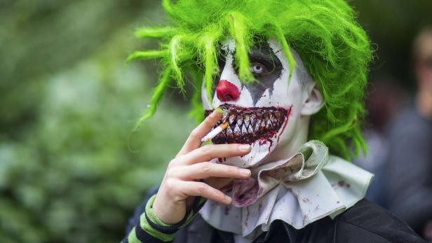Ein gruseliger Clown mit grünen Haaren und blutigem Make-up raucht eine Zigarette.