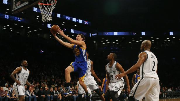 Ein Basketballspieler in blau-gelber Uniform springt, um den Ball in den Korb zu werfen.