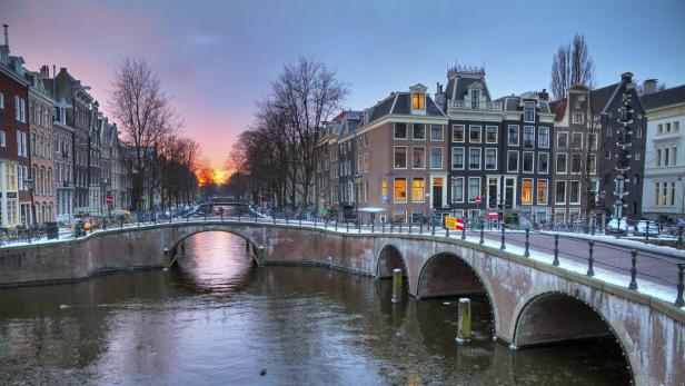 Eine Brücke überspannt einen Kanal in Amsterdam bei Sonnenaufgang.