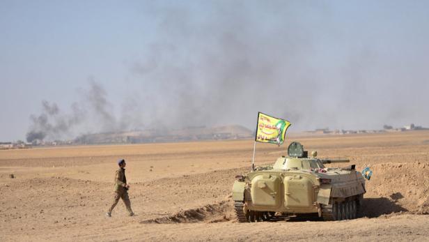 Ein Soldat geht an einem Panzer mit einer Flagge in einer Wüstenlandschaft vorbei.