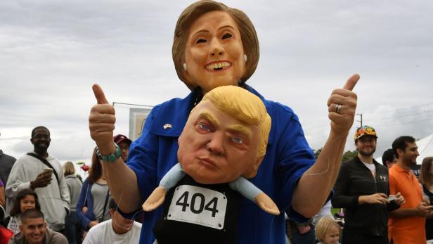 Eine Person in einer Hillary-Clinton-Maske hält eine Donald-Trump-Puppe mit der Nummer 404 hoch und zeigt mit beiden Daumen nach oben.