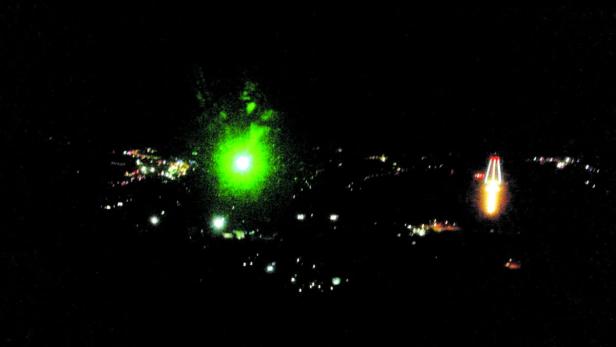 Nachts leuchten grüne und rote Lichter über einer Stadt.