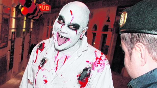 Ein Mann mit Zombie-Make-up und blutverschmiertem Hemd steht vor einem Pub.