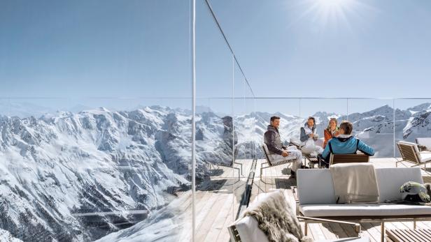 Eine Gruppe von Menschen sitzt auf einer Terrasse mit Blick auf schneebedeckte Berge.