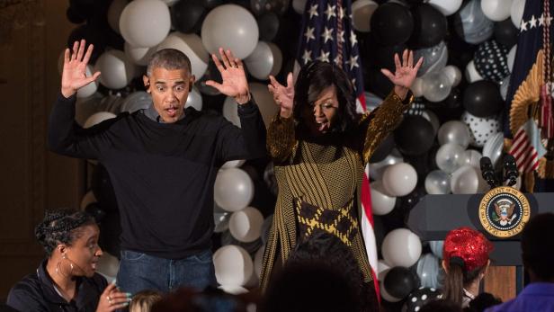 Barack und Michelle Obama mit erhobenen Händen vor einem Hintergrund aus Ballons.