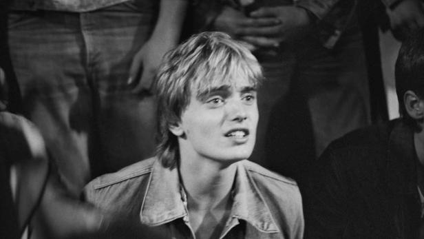 Ein junger Mann mit blonden Haaren und Jeansjacke schaut aufmerksam nach oben.