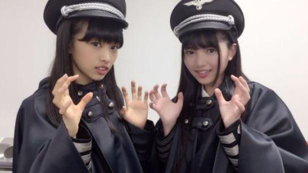 Zwei junge Frauen in Uniformen und Mützen posieren mit ausgestreckten Händen.