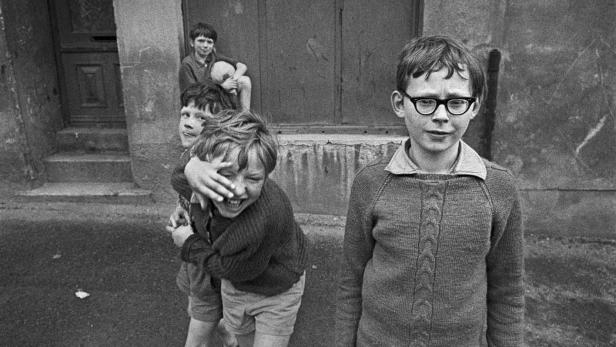 Eine Gruppe Jungen spielt in einer Gasse, einer davon trägt eine Brille.