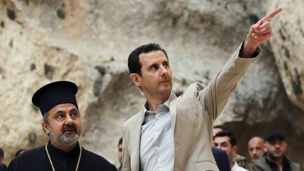 Baschar al-Assad mit erhobenem Zeigefinger neben einem orthodoxen Priester.