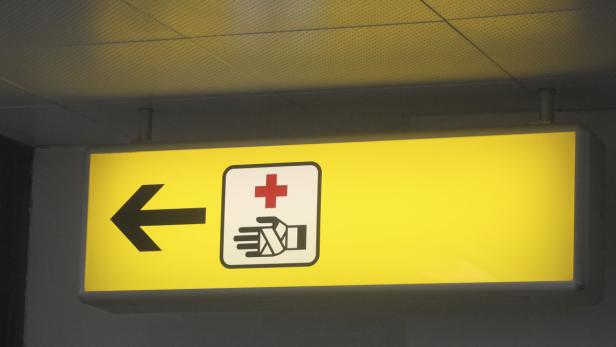 Ein gelbes Schild mit einem Pfeil nach links und einem Symbol für Erste Hilfe.