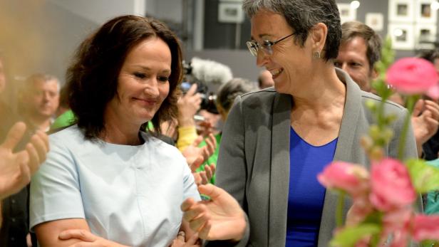 Zwei Frauen stehen lächelnd im Gespräch, umgeben von Menschen und Blumen.