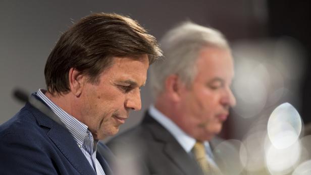 Zwei Männer in Anzügen sitzen nebeneinander.