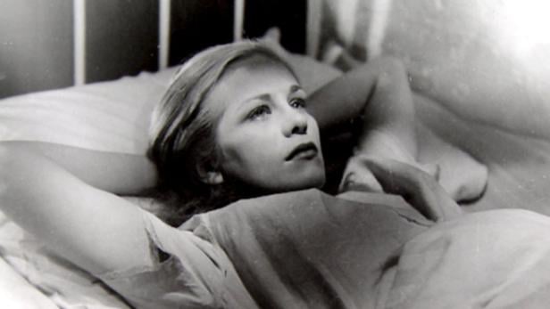 Eine junge Frau liegt in einem Bett und schaut nach oben.