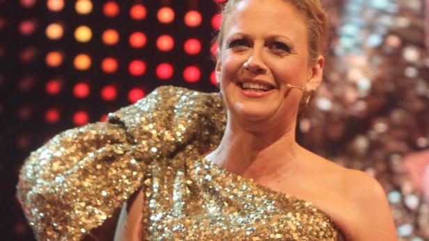 Eine Frau in einem goldenen Paillettenkleid hält eine „25 Jahre OMY 2014“-Karte.