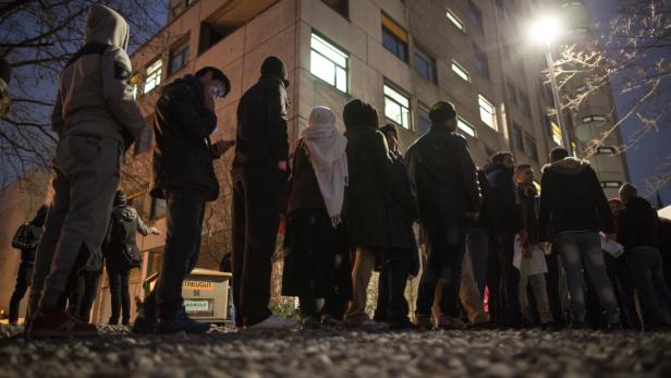 Eine Gruppe von Menschen steht abends vor einem Gebäude.