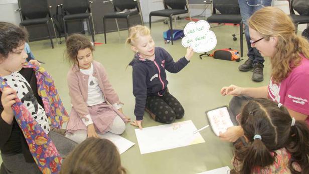 Eine Gruppe Kinder sitzt mit einer Betreuerin auf dem Boden und spielt ein Spiel.