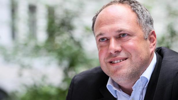Ein Mann in einem dunklen Anzug lächelt in die Kamera.