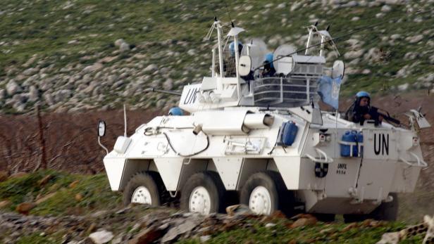 Ein weißer UN-Panzerwagen fährt durch eine hügelige Landschaft.