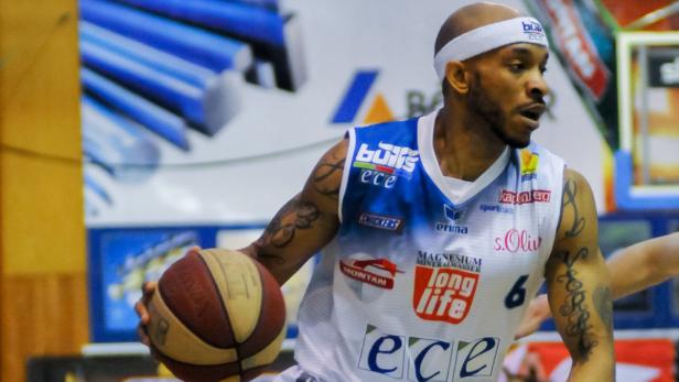 Ein tätowierter Basketballspieler mit Stirnband dribbelt den Ball.