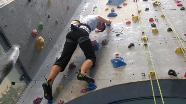 Eine Frau klettert an einer Kletterwand mit farbigen Griffen.
