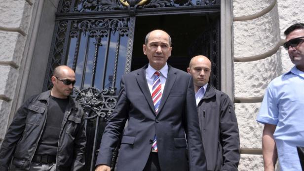 Ein Mann in einem Anzug wird von mehreren Leibwächtern begleitet.