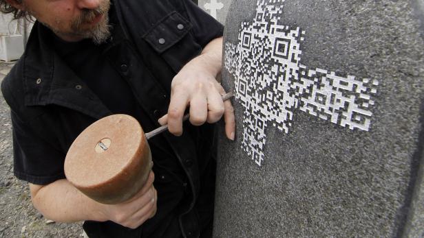 Ein Steinmetz graviert mit Hammer und Meißel einen QR-Code in einen Grabstein.