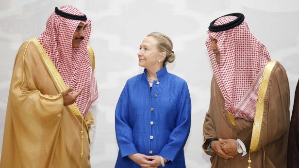 Hillary Clinton steht zwischen zwei Männern in traditioneller arabischer Kleidung.