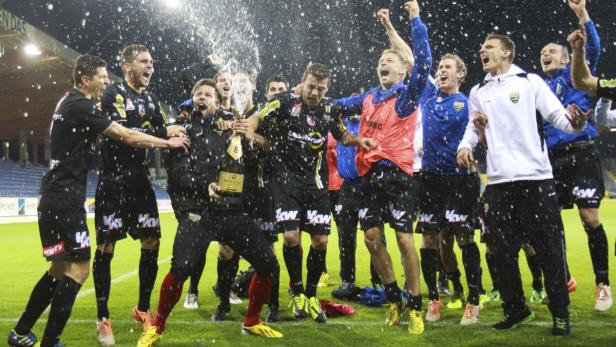 Eine Fußballmannschaft feiert mit einer Champagnerdusche auf dem Rasen.