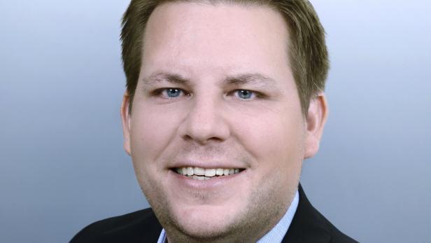 Ein lächelnder Mann mit hellblauen Augen und einem dunklen Anzug.