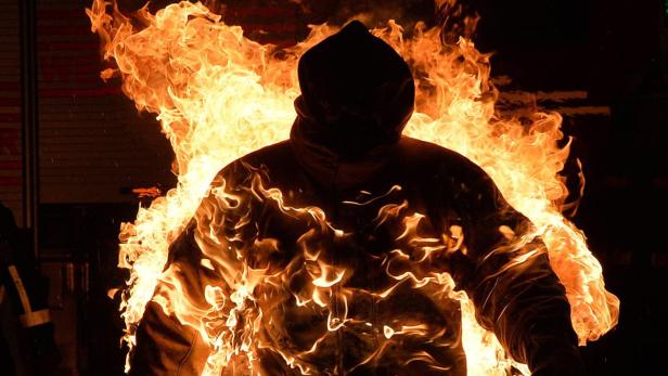 Eine Person in Flammen steht vor einem dunklen Hintergrund.
