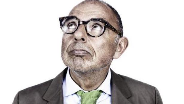Ein Mann mit Brille, Anzug und grüner Krawatte blickt nach oben.