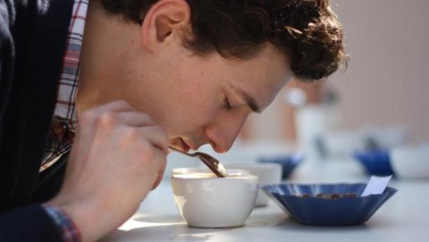 Ein Mann probiert Kaffee mit einem Löffel aus einer weißen Tasse.