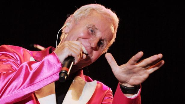Howard Carpendale tritt in einem pinkfarbenen Sakko mit Mikrofon auf.