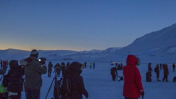 Eine Gruppe von Menschen beobachtet eine Sonnenfinsternis in einer verschneiten Landschaft.