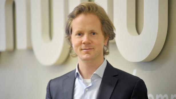 Ein Mann mit blonden Haaren und einem dunklen Anzug lächelt in die Kamera.