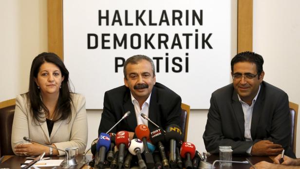 Drei Personen sitzen vor einem Schild mit der Aufschrift „Halkların Demokratik Partisi“.